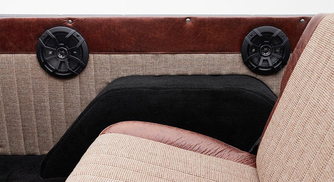 Two black speakers on brown and beige checkered panel behind tan and brown seat inside Classic Ford Bronco
