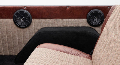 Two black speakers on brown and beige checkered panel behind tan and brown seat inside Classic Ford Bronco