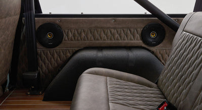 Two black round speakers with yellow centers mounted on quilted brown interior panel with beige seat