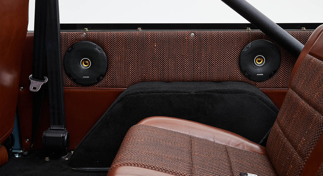 Speakers mounted on the interior side panel behind a brown leather car seat with woven detailing.