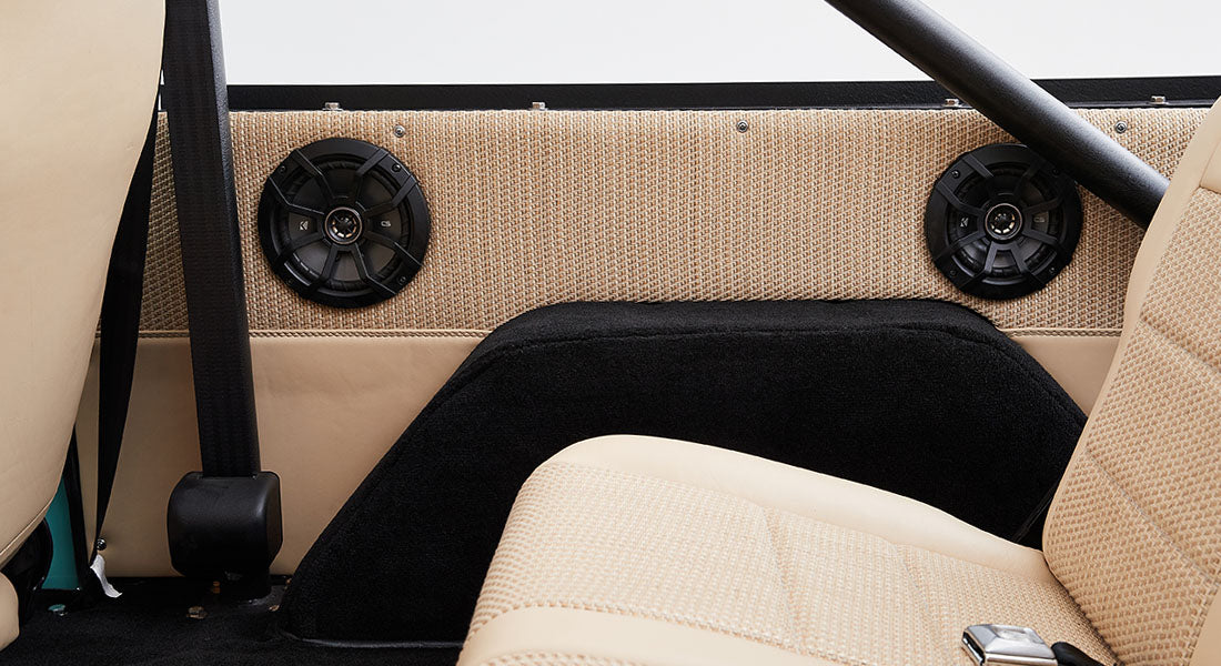 Interior view of Classic Ford Bronco rear with beige woven fabric panels and black round speakers.