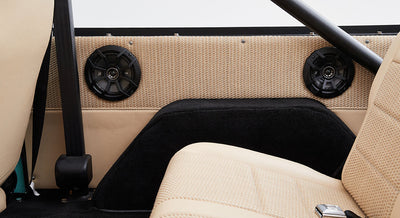 Interior view of Classic Ford Bronco rear with beige woven fabric panels and black round speakers.