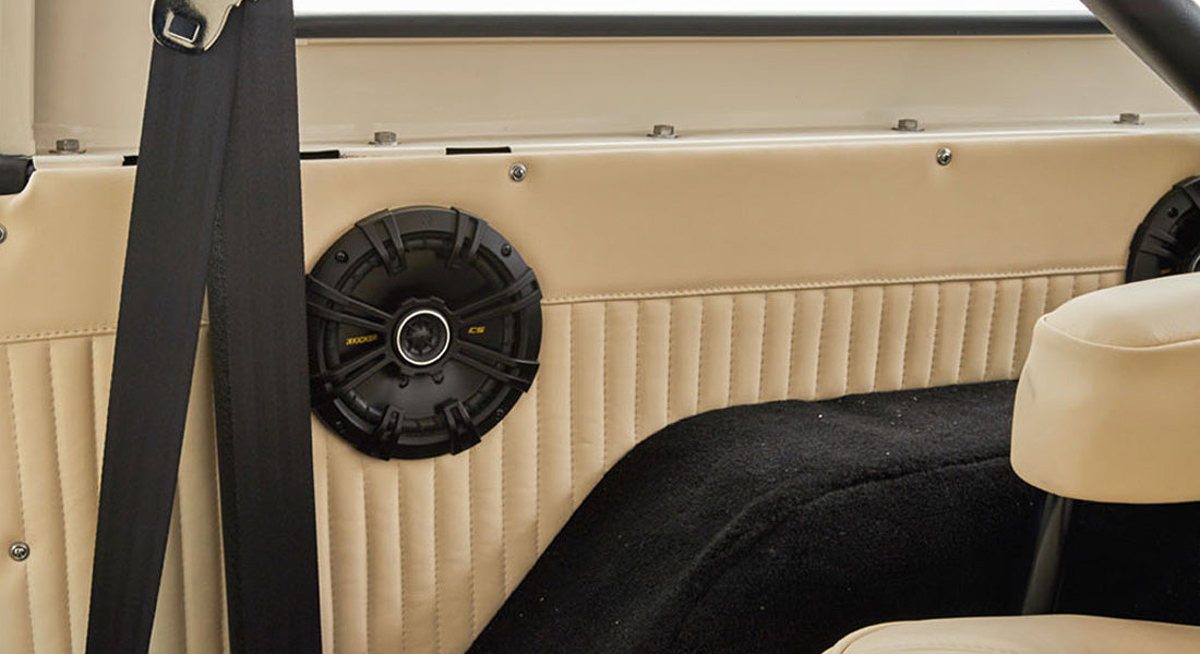 Black round speaker mounted on beige panel with seatbelt and light upholstery inside vehicle