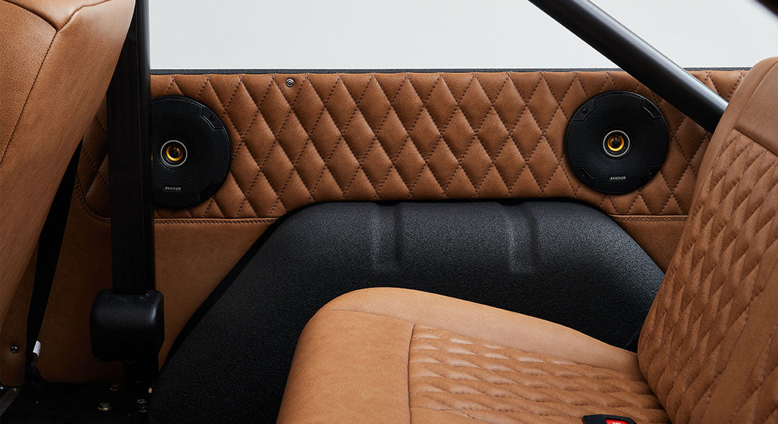 Two round black speakers mounted on a tan quilted leather panel inside a Classic Ford Bronco