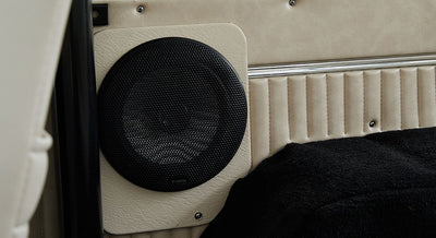 Black speaker mounted on beige panel inside a Classic Ford Bronco above carpeted floor