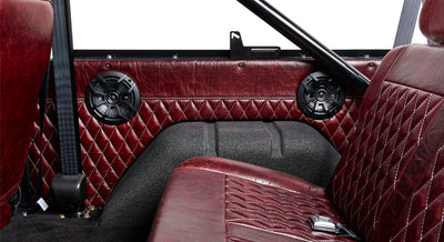Rear interior side panel of Classic Ford Bronco with red diamond-stitched upholstery and black round speaker.