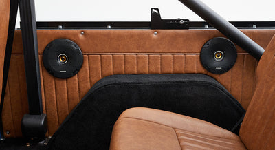 Two black speakers mounted on a brown leather interior panel of a Classic Ford Bronco