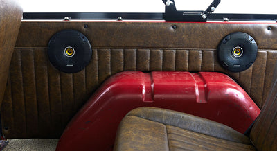 Two round black speakers mounted in the brown leather interior panel of a Classic Ford Bronco