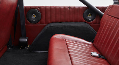 Two round speakers mounted on red leather interior side panel with passenger seat