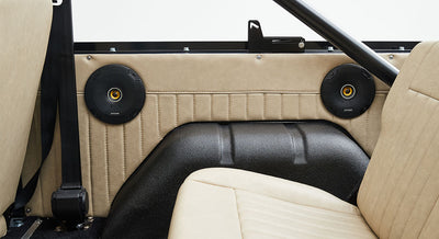 Two black speakers mounted on beige interior panel behind tan passenger seat