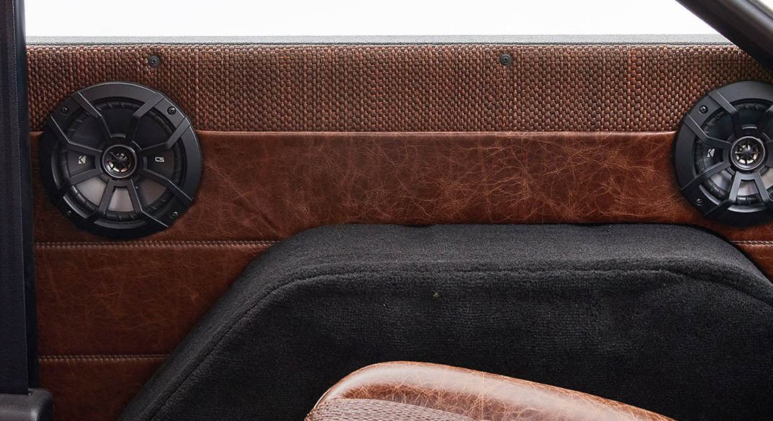 Pair of round black speakers mounted in brown textured and stitched interior panel