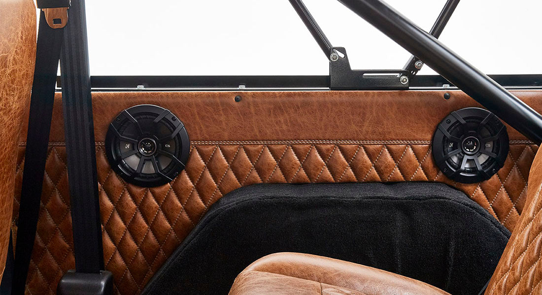 Pair of black speakers mounted on brown quilted leather interior panel with seatbelt
