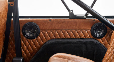 Pair of black speakers mounted on brown quilted leather interior panel with seatbelt