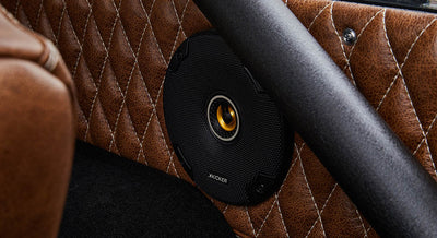 Close-up of one black speaker with yellow cone center on diamond-stitched brown leather panel