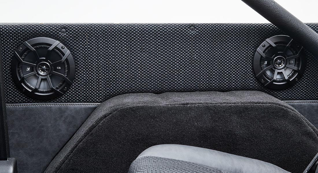 Two black speakers mounted on the black textured dashboard of Classic Ford Bronco