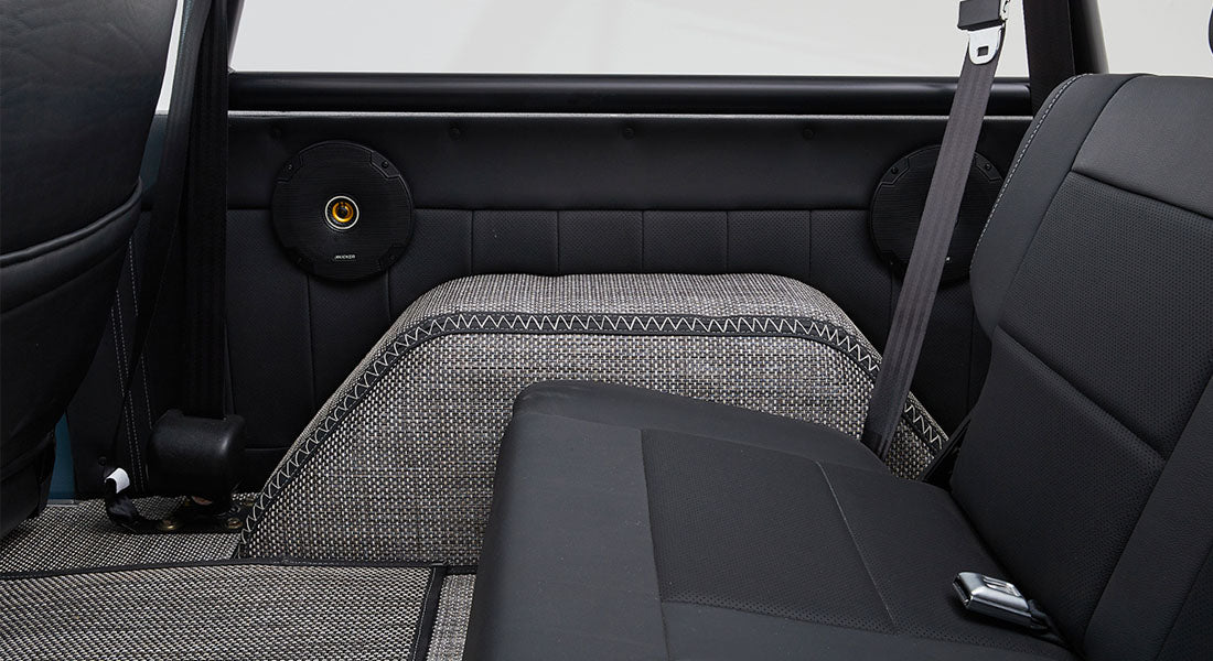 Rear interior view of classic Ford Bronco showing back seat, speakers, and patterned floor covering