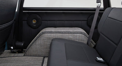 Rear interior view of classic Ford Bronco showing back seat, speakers, and patterned floor covering