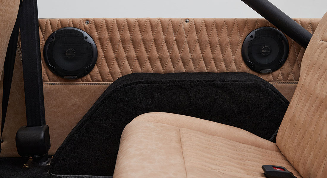 Tan quilted upholstery with black speaker grills and part of a seatback in a Classic Ford Bronco