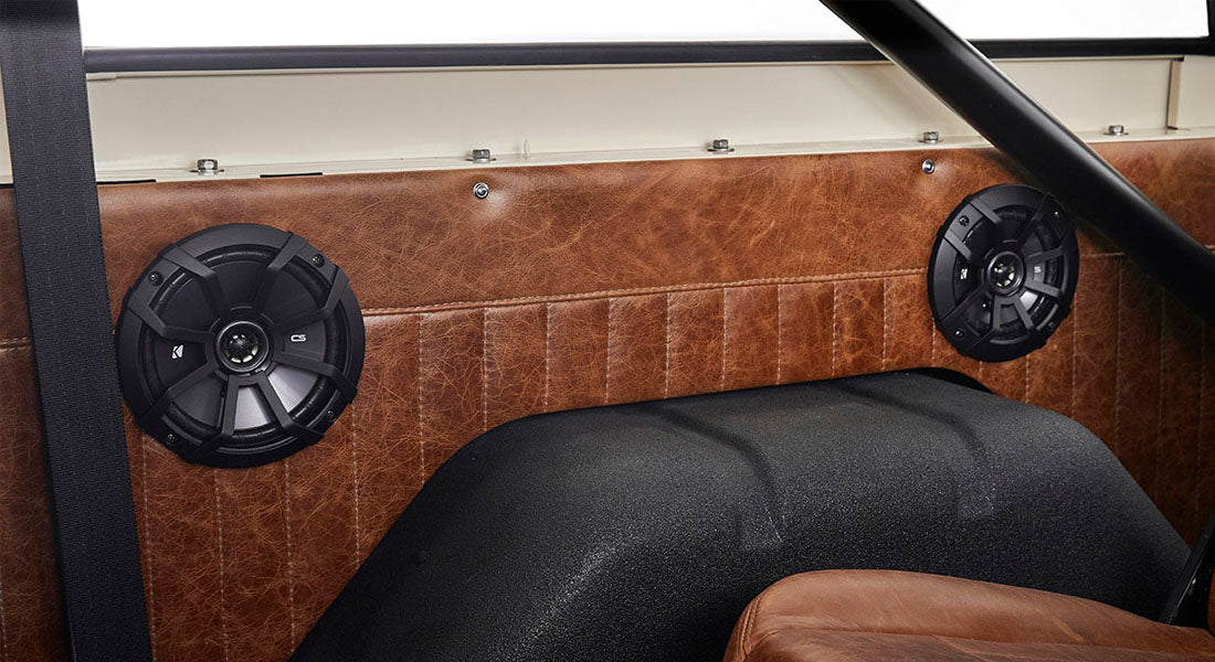 Two black circular speakers mounted on brown leather interior of Classic Ford Bronco