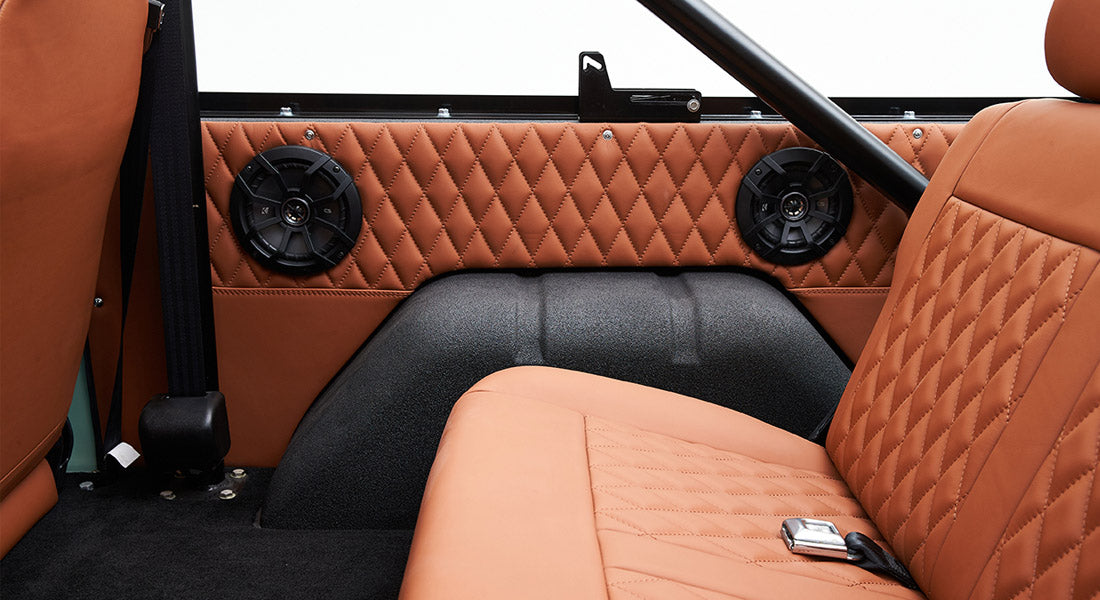 Classic Ford Bronco rear interior with tan quilted upholstery and two black speakers installed on the side panel.