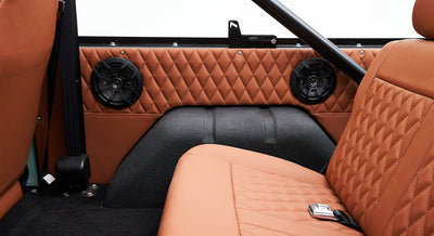 Classic Ford Bronco rear interior with tan quilted upholstery and two black speakers installed on the side panel.