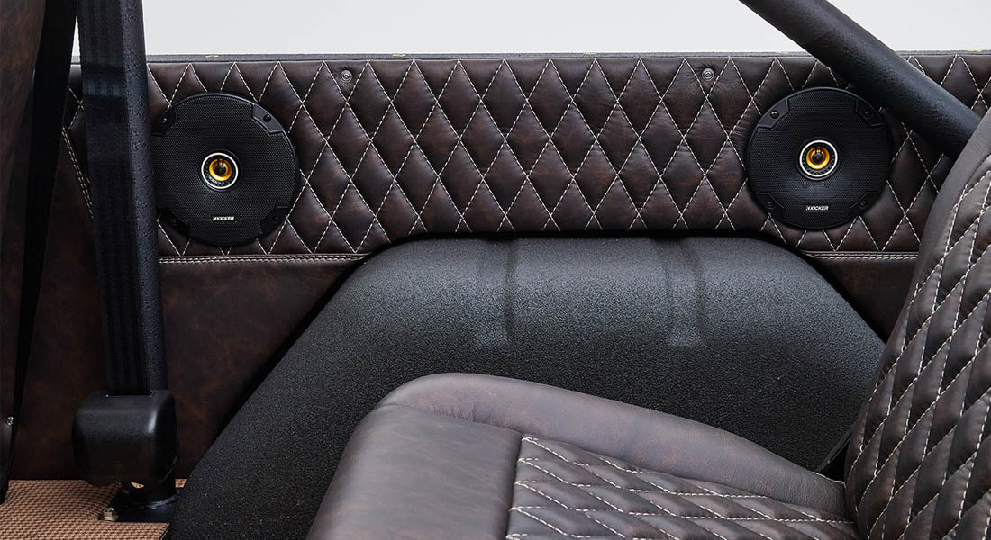 Two round black speakers with orange accents installed on quilted brown leather interior