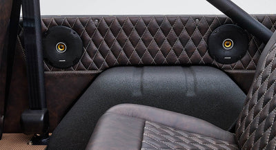 Two round black speakers with orange accents installed on quilted brown leather interior