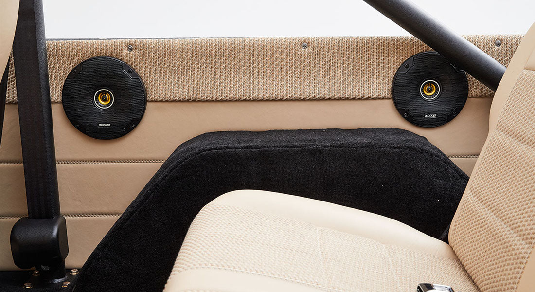 Two round black speakers installed on beige interior panel behind the seats