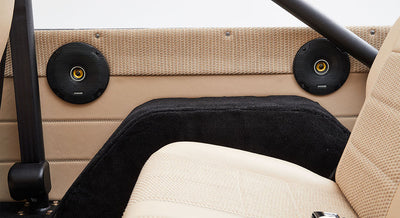 Two round black speakers installed on beige interior panel behind the seats
