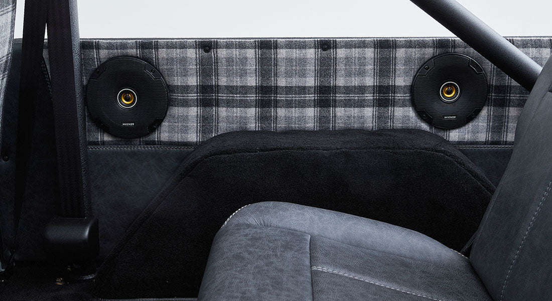Rear interior of a Classic Ford Bronco showing plaid fabric, speakers, and roll bar