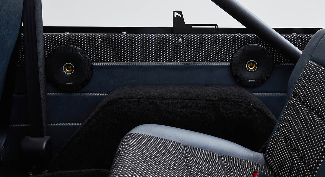 Two black circular Kicker speakers installed on black and blue rear interior panels of vehicle