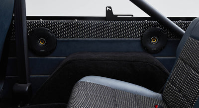 Two black circular Kicker speakers installed on black and blue rear interior panels of vehicle