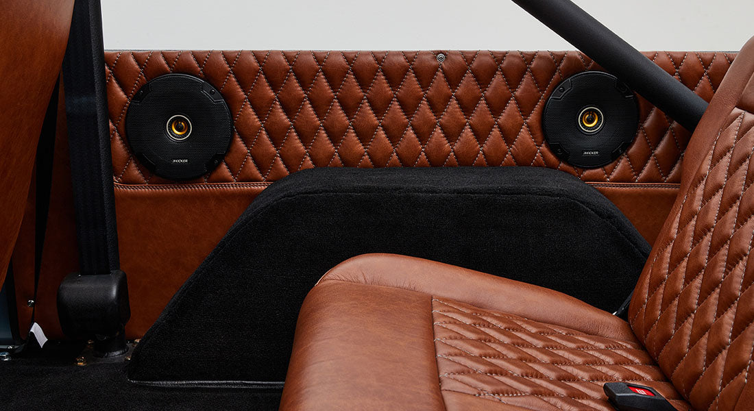 Rear interior side panel with two black round speakers and brown quilted leather seats of a Classic Ford Bronco