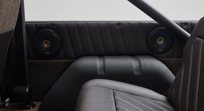 Interior rear side panel with black speakers, brown upholstery, and padded roll cage of Classic Ford Bronco