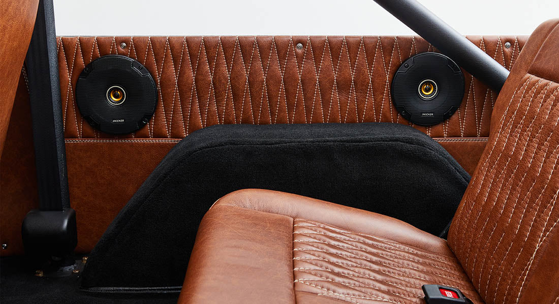 Two black speakers mounted on brown leather interior panels inside a Classic Ford Bronco