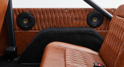 Two black speakers mounted on brown leather interior panels inside a Classic Ford Bronco