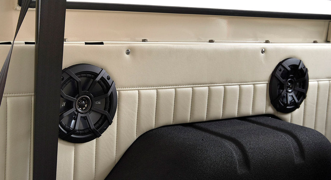 Two black speakers mounted on the cream-colored interior panel of a Classic Ford Bronco