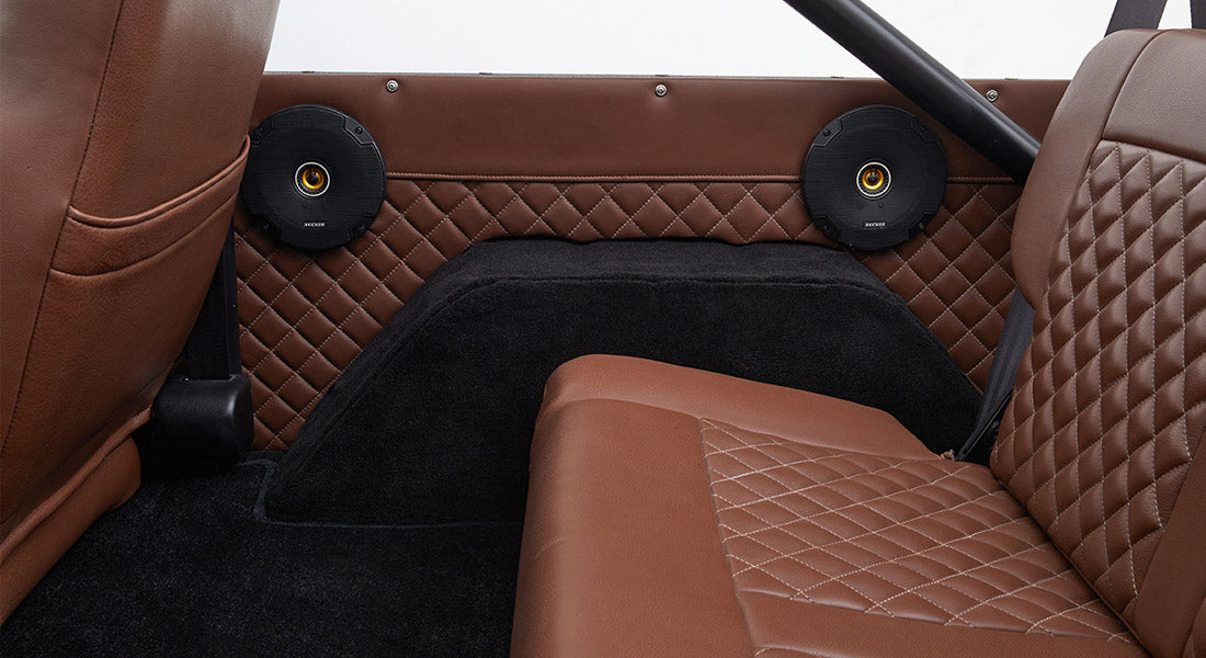 Rear interior side panel with two round black speakers and brown diamond-stitched leather in Classic Ford Bronco.