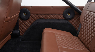 Rear interior side panel with two round black speakers and brown diamond-stitched leather in Classic Ford Bronco.
