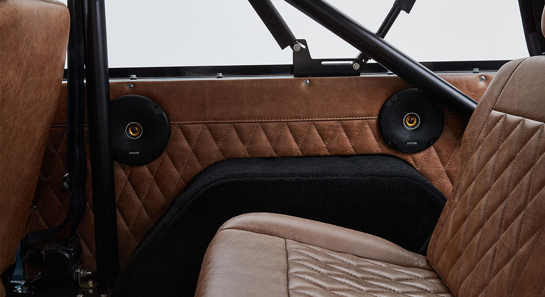 Two black Kicker speakers installed on tan quilted leather interior panels inside a Classic Ford Bronco