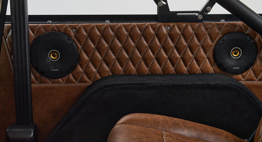 Two black round speakers mounted on diamond-stitched brown leather rear panel