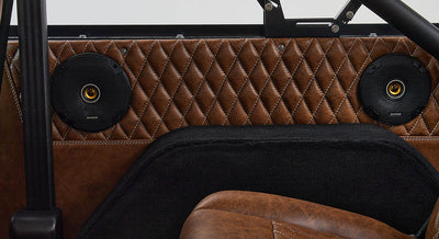 Two black round speakers mounted on diamond-stitched brown leather rear panel