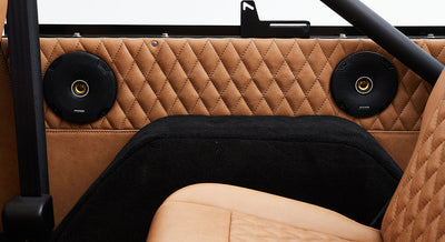 Two black circular speakers mounted on diamond-stitched tan leather inside a Classic Ford Bronco.