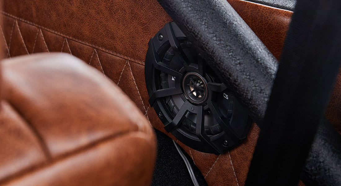 Black speaker mounted on brown leather interior panel with quilted stitching