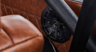 Black speaker mounted on brown leather interior panel with quilted stitching