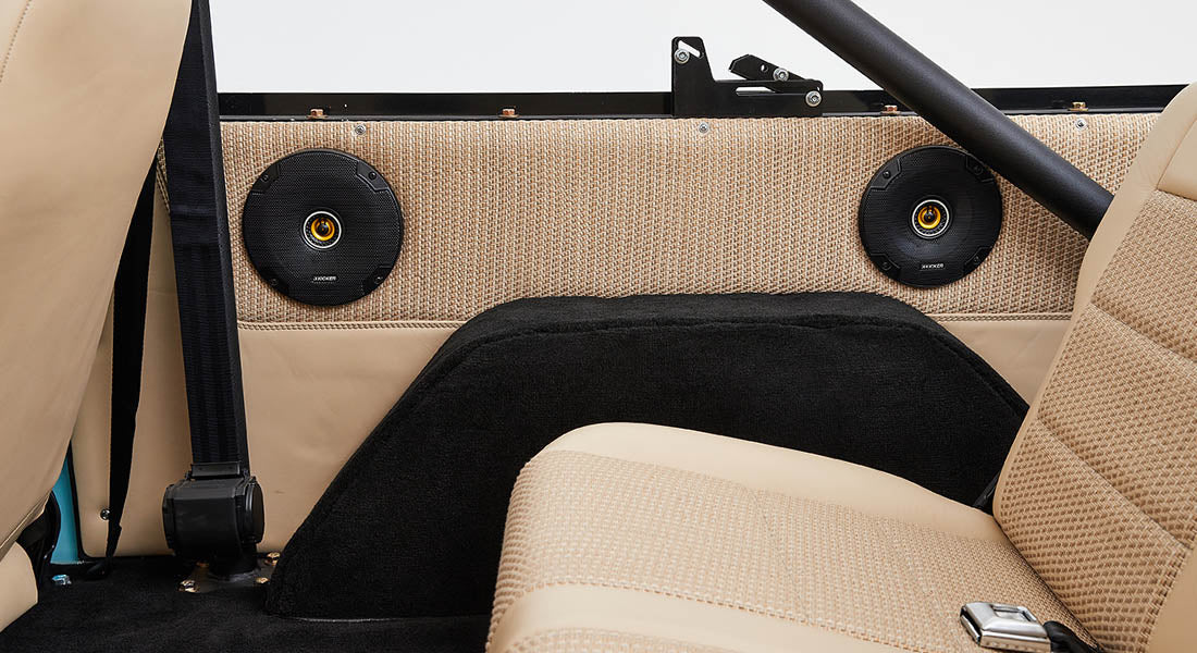 Pair of black round speakers mounted on a tan and black vehicle panel near seats