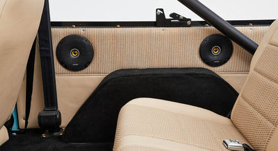 Pair of black round speakers mounted on a tan and black vehicle panel near seats
