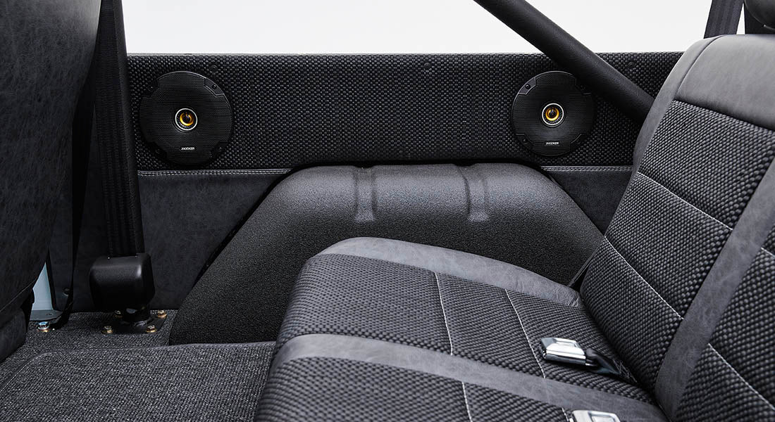 Classic Ford Bronco rear interior with black upholstery and two black round speakers on side panels.
