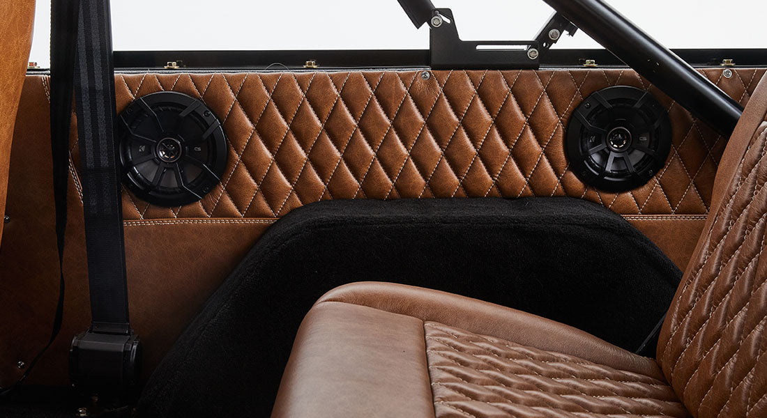 Brown leather interior panel of Classic Ford Bronco with two black round speakers and seatbelt