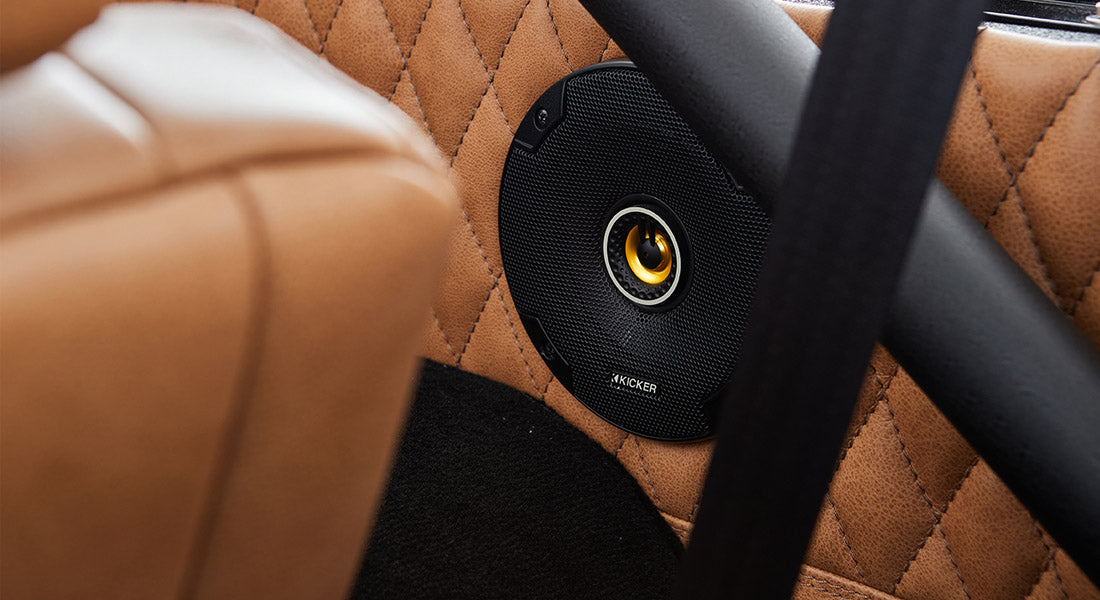 Close-up of black speaker grille mounted on diamond-stitched tan leather panel inside Classic Ford Bronco.